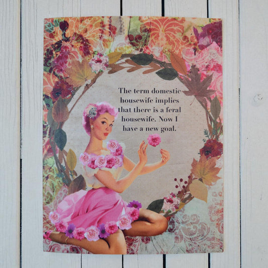 A vintage-style illustrated print or card featuring a woman in a pink dress seated among floral wreath elements, with black text in the center reading, 'The term domestic housewife implies that there is a feral housewife. Now I have a new goal.