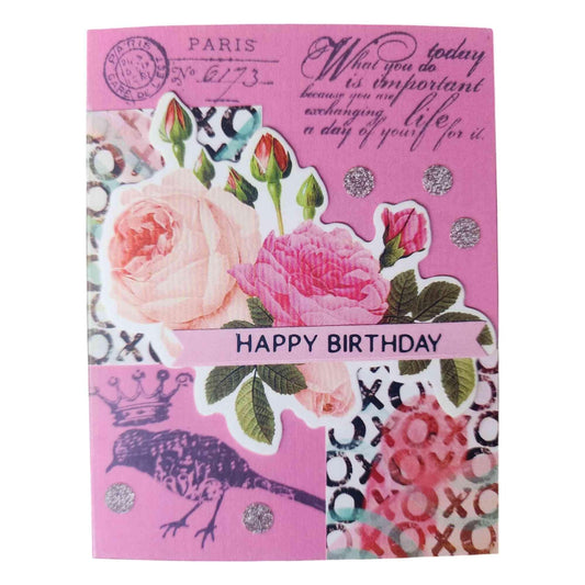 A pink birthday card featuring a collage of vintage-style designs, including pink roses, postmark stamps, silver glitter circles, a bird silhouette, and decorative text including 'HAPPY BIRTHDAY'.